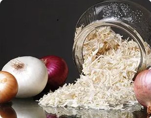 Dehydrated white onion flakes spilling from a glass jar beside fresh onions